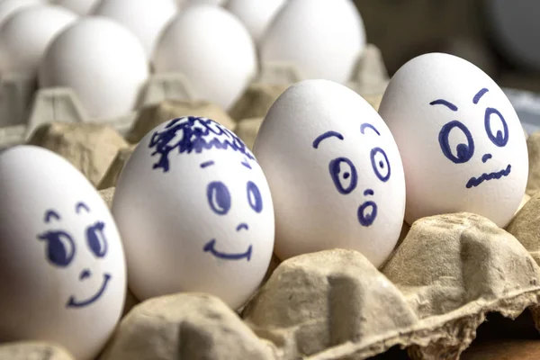 Preciosos huevos en caja de cartón. Huevos con emociones. Huevos blancos en caja de cartón con diferentes caras pintadas sobre ellos. Niños y niñas — Foto de Stock