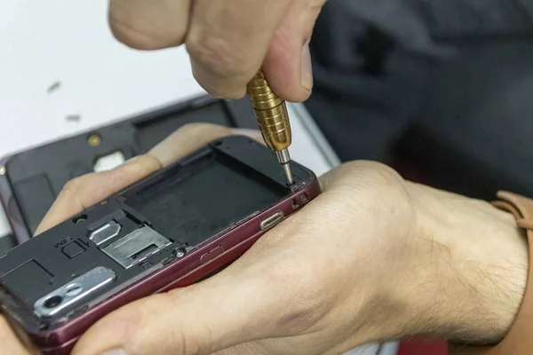 Ancianos y jóvenes reparan un teléfono móvil juntos. Trabajan en un taller de reparación. Utilizan diferentes herramientas. Son especialistas en reparaciones. —  Fotos de Stock