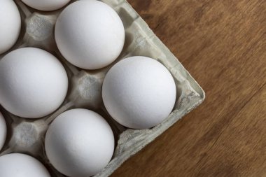 Tavuk yumurtası tepsiye çiğ vardır. Kabuk yumurtalar beyaz. Bir bölümde bir yumurta kabuğu. Bir yumurta üzerinde beyaz renk bir tüy yatıyor. Ahşap arka plan. Yukarıdan görüntüle. Close.