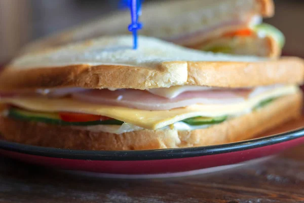 Close-up photo of a club sandwich. Sandwich with meet, prosciutto, salami, salad, vegetables, lettuce, tomato, onion and mustard on a fresh sliced rye bread on wooden background.