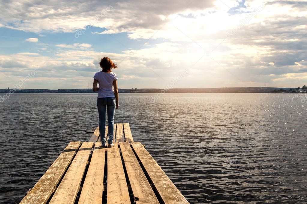 A girl is standing on a wooden pier on the background of the sea