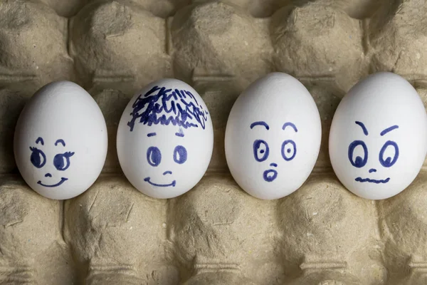 Preciosos huevos en caja de cartón. Huevos con emociones. Huevos blancos en caja de cartón con diferentes caras pintadas sobre ellos. Niños y niñas — Foto de Stock