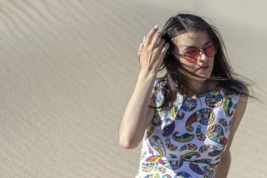 Çölde kum üzerinde oturan güzel bir genç kız, kum tepeleri