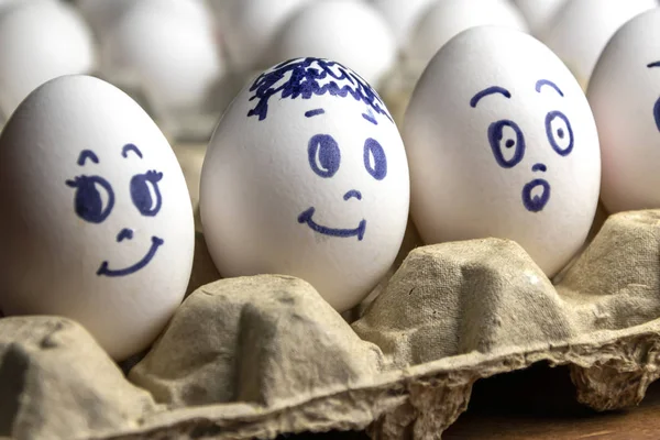 Preciosos huevos en caja de cartón. Huevos con emociones. Huevos blancos en caja de cartón con diferentes caras pintadas sobre ellos. Niños y niñas — Foto de Stock