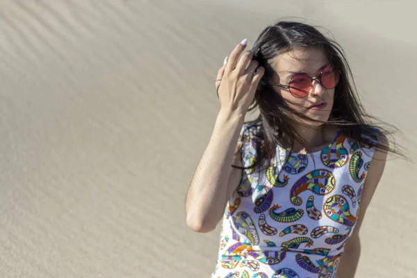 Çölde kum üzerinde oturan güzel bir genç kız, kum tepeleri