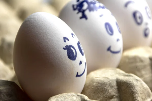 Preciosos huevos en caja de cartón. Huevos con emociones. Huevos blancos en caja de cartón con diferentes caras pintadas sobre ellos. Niños y niñas — Foto de Stock