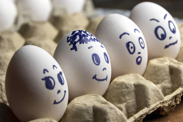 Preciosos huevos en caja de cartón. Huevos con emociones. Huevos blancos en caja de cartón con diferentes caras pintadas sobre ellos. Niños y niñas — Foto de Stock