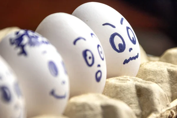 Preciosos huevos en caja de cartón. Huevos con emociones. Huevos blancos en caja de cartón con diferentes caras pintadas sobre ellos. Niños y niñas — Foto de Stock