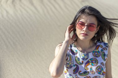 Çölde kum üzerinde oturan güzel bir genç kız, kum tepeleri