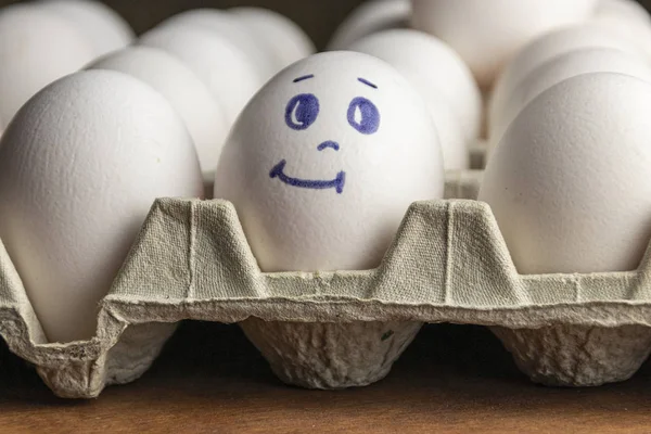 Preciosos huevos en caja de cartón. Huevos con emociones. Huevos blancos en caja de cartón con diferentes caras pintadas sobre ellos. Niños y niñas . — Foto de Stock