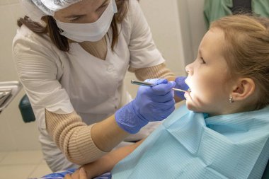 Küçük beyaz kız dişçide dişlerini tedavi ediyor.