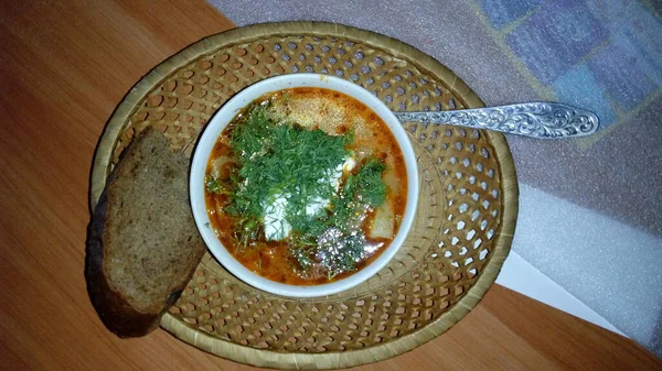 Deliciosa sopa con todos los condimentos en un plato pequeño en un plato de mimbre sobre la mesa — Foto de Stock