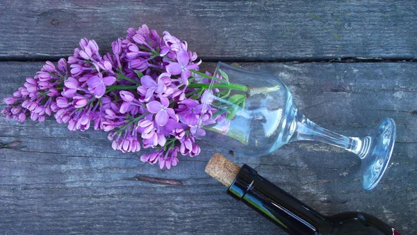 A bottle of wine and a sprig of lilac on a wooden background.