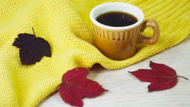 Bir fincan kahve ve sarı bir arka plan üzerinde renkli sonbahar yaprakları.