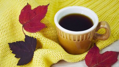 Bir fincan kahve ve sarı bir arka plan üzerinde renkli sonbahar yaprakları.
