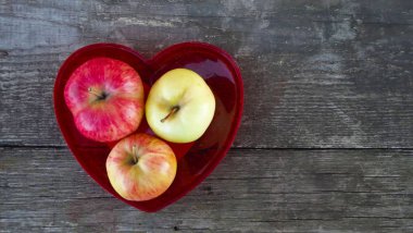 Ahşap arka plan üzerinde kırmızı kalp şeklinde vazoda taze tatlı elma.
