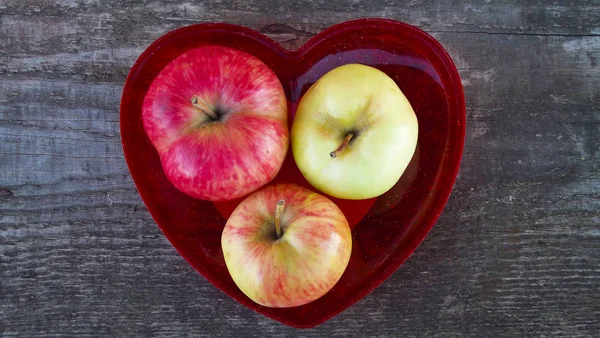 Fresh sweet apples in red heart shaped vase on wooden background.