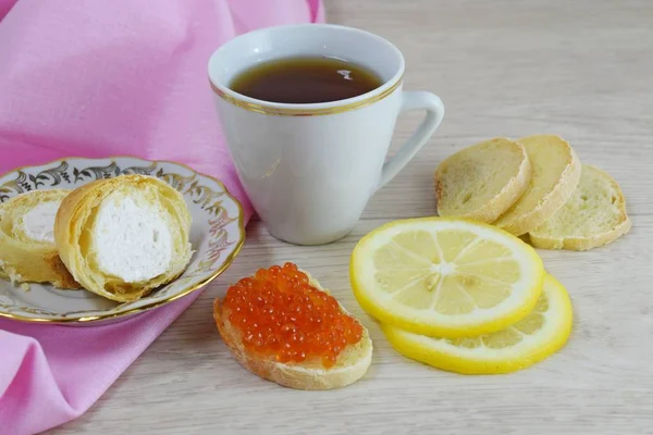 Fragrant tea with lemon and a sandwich with red caviar.Delicious cake on a white plate.