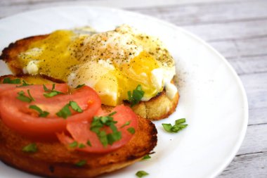 Çıtır çıtır kızarmış ekmek, sahanda yumurta ve domates kahvaltıda beyaz bir plaka üzerinde.