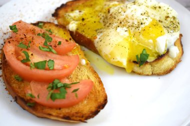 Çıtır çıtır kızarmış ekmek, sahanda yumurta ve domates kahvaltıda beyaz bir plaka üzerinde.