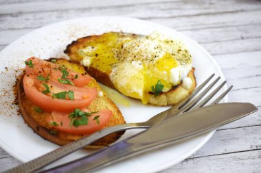 Çıtır çıtır kızarmış ekmek, sahanda yumurta ve domates kahvaltıda beyaz bir plaka üzerinde.