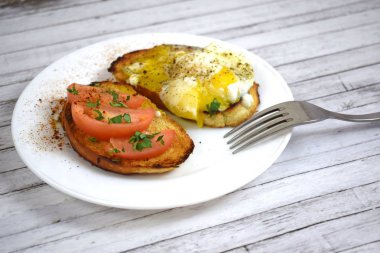 Çıtır çıtır kızarmış ekmek, sahanda yumurta ve domates kahvaltıda beyaz bir plaka üzerinde.