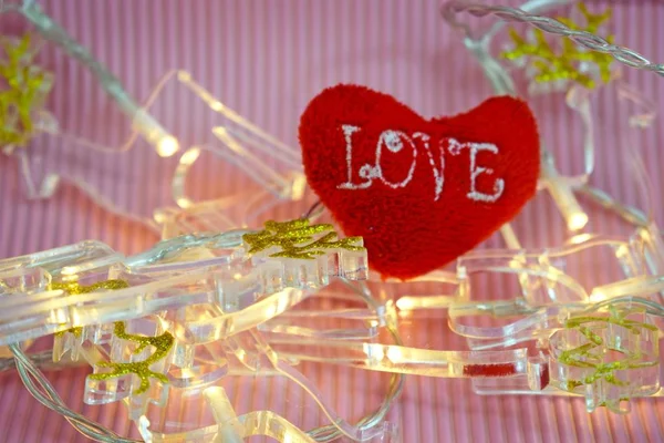 Valentine`s day.Red heart and lights garland on pink background.