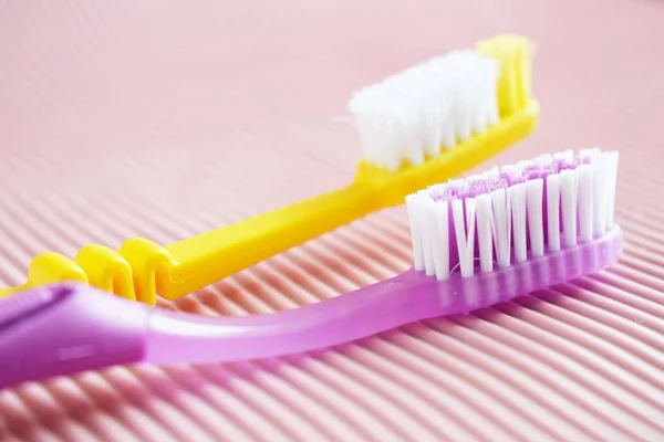 Yellow and purple toothbrush on pink background.