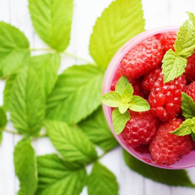 Bir Fincan taze, olgun ahududu ve beyaz bir arka plan üzerinde yeşil ahududu yaprakları.