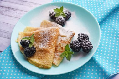 Ahşap bir arka plan üzerinde böğürtlen ve nane ile lezzetli sıcak krep.