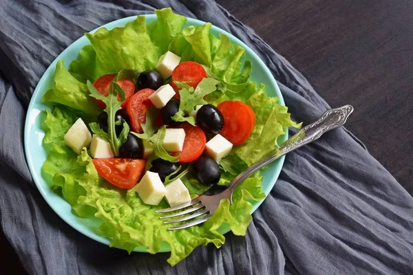 Light salad with tomato greens and cheese on a blue plate.Vegetarian food.