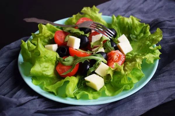Light salad with tomato greens and cheese on a blue plate.Vegetarian food.