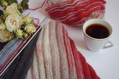 Bir fincan mis kokulu kahve ve beyaz bir arka planda örgü iğneleriyle örülmüş bir eşarp..