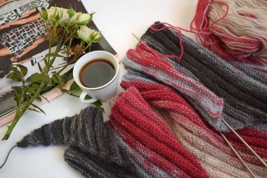 Bir fincan mis kokulu kahve ve beyaz bir arka planda örgü iğneleriyle örülmüş bir eşarp..