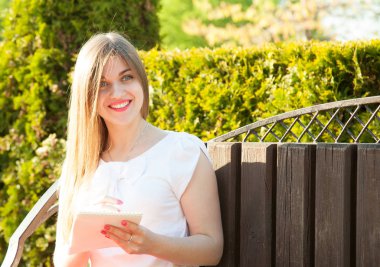 Sevimli genç kadın bir yaz parkta bir bankta oturmuş bir günlüğüne notlar yapma