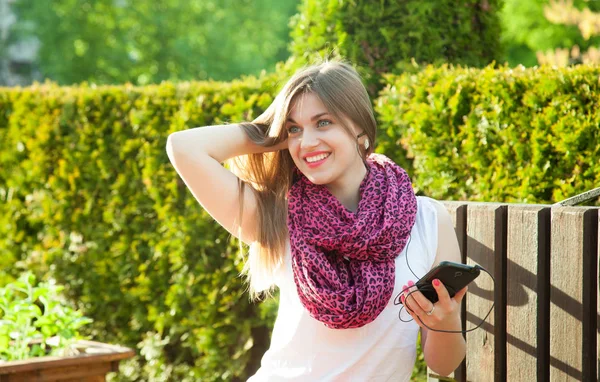 美丽的微笑的学生女孩听音乐在她的手机坐在一个夏天的公园 — 图库照片