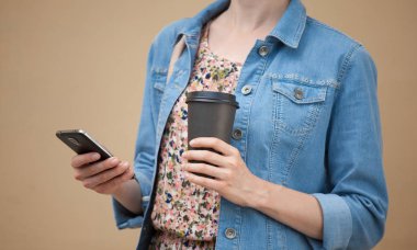 Bir fincan kahve ve cep telefonu açık havada tanınmaz halde genç kadın