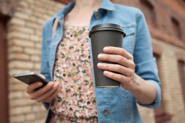 Bir fincan kahve ve cep telefonu açık havada tanınmaz halde genç kadın