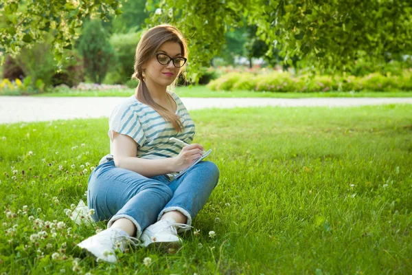 Muito Jovem Estudante Fazendo Anotações Diário Sentado Gramado Ensolarado Parque — Fotografia de Stock