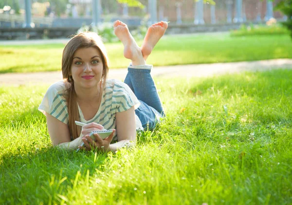 日当たりの良い草原に横たわっている日記のノートを作る美しい若い女性 — ストック写真