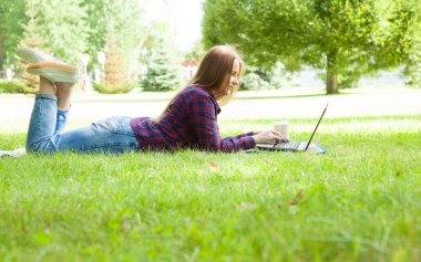 Bir yaz parkta çim üzerinde yalan dizüstü bilgisayarda çalışan güzel genç kadın