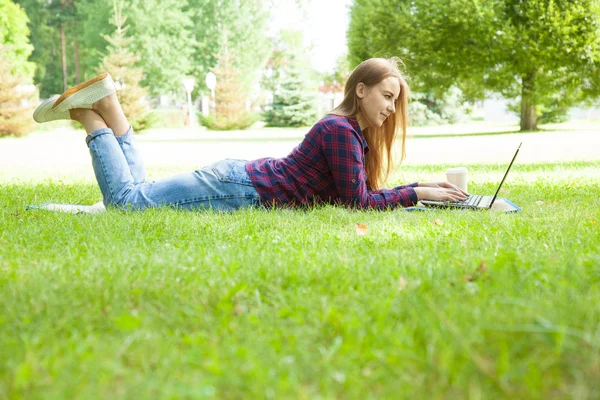 Bir yaz parkta çim üzerinde yalan dizüstü bilgisayarda çalışan çekici genç kadın