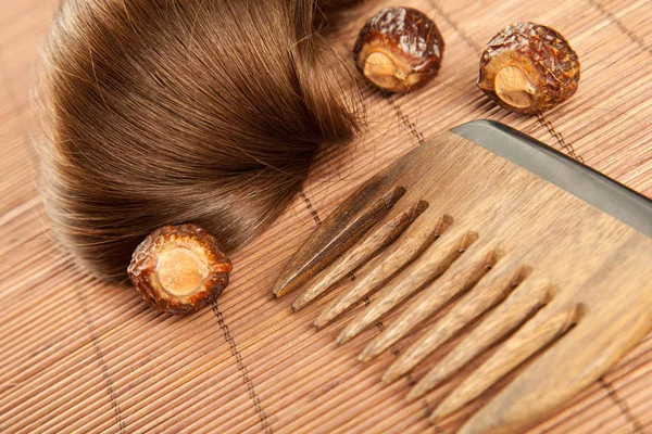 Hair lock, soapnuts and wooden comb on bamboo background; haircare concept