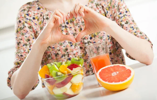 在桌前展示心脏标志的认不出来的年轻女子 用新鲜的水果做早餐 说明她对健康生活方式的立场 — 图库照片