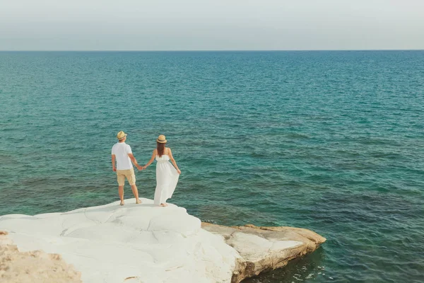 back view of romantic young couple watching sea from white stony shore in Cyprus