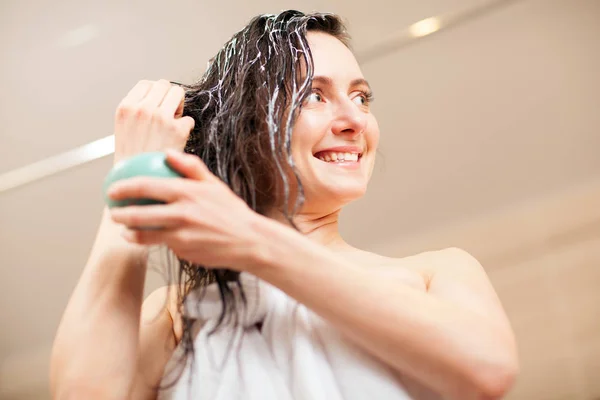 Mujer joven sonriente aplicando mascarilla para el cabello en un baño —  Fotos de Stock