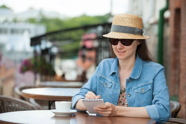 コーヒーを飲みながら夏のカフェに座って 日記にメモを取る魅力的な若い女性 — ストック写真