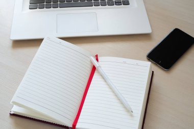 Beyaz dizüstü, açık defter, kalem ve telefon masa lambası. 