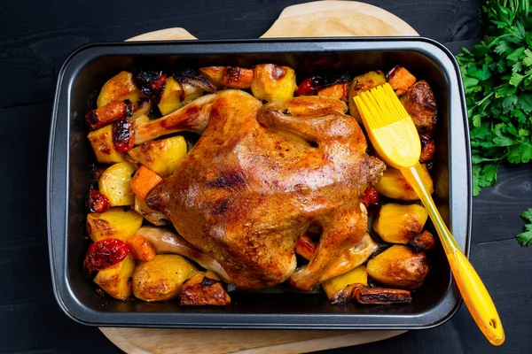 Baked chicken with vegetables on a black wooden background. Top of view