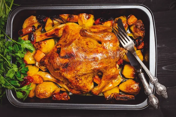 Fried chicken with vegetables on a black wooden background. Next old fork and knife. Top of view, toned.